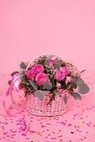 romantisk bukett av rosa ro och eukalyptus i en korg på en rosa bakgrund med konfetti. födelsedag gåva, kvinnors dag, mammas dag, hjärtans dag foto