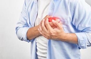asiatisk man i blå skjorta bröst smärta lidande från en hjärta ge sig på på vit bakgrund foto
