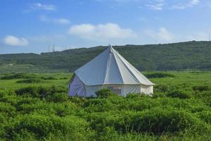 vitt tält i ett fält med molnig blå himmel foto