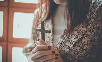 en kvinna ber och håller ett kors foto