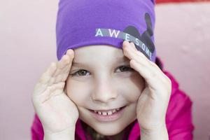 porträtt av en glad förskola flicka i en lila hatt. foto