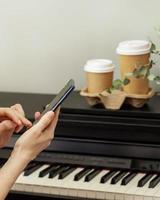 kvinna händer innehav smartphone innan piano med två koppar av kaffe foto