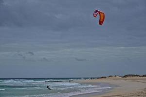 sommar landskap med de hav med mörk molnig vågor och surfermi utrustning med fallskärmar flytande på de Strand foto