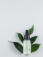 glas flaska av kosmetisk serum och grön löv på en ljus bakgrund foto