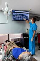 manlig mitten -åldrig tandläkare på hans kontor använder sig av ett x stråle bild till förklara behandling till hans senior kvinna patient foto