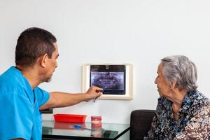 manlig mitten -åldrig tandläkare på hans kontor använder sig av ett x stråle bild till förklara behandling till hans senior kvinna patient foto