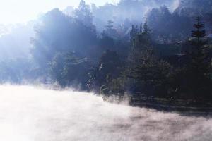 skön landskap himmel av dimma och dimma över de sjö och soluppgång lysande med blå himmel reflexion på de vatten yta på kulle stam by på berg i thailand foto