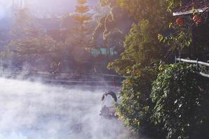 skön landskap himmel av dimma och dimma över de sjö och soluppgång lysande med blå himmel reflexion på de vatten yta på kulle stam by på berg i thailand foto