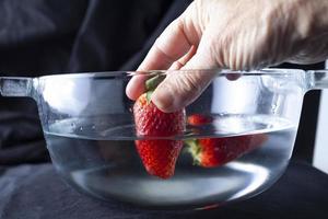 person som sätter jordgubbar i vatten foto