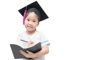 Lycklig asiatisk skola unge examen skrivning bok med gradering keps foto