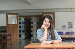 självsäker leende studerande asiatisk flicka i de bibliotek foto