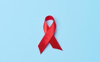 en silke röd band i de form av en rosett på en blå bakgrund, en symbol av de bekämpa mot AIDS och en tecken av solidaritet och Stöd foto