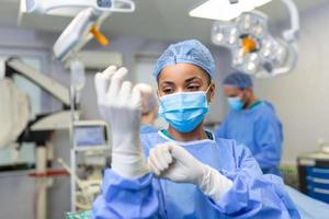 porträtt av skön kvinna läkare kirurg sätta på medicinsk handskar stående i drift rum. kirurg på modern rörelse rum foto