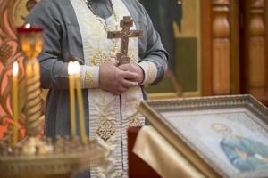 prästens hand med en korsa på de bakgrund av kyrka ljus. foto