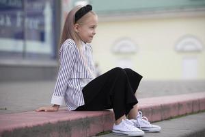 en liten flicka sitter på en trottoarkant i ett urban miljö. foto