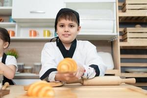 porträtt av en liten pojke i de kök av en hus har roligt spelar bakning bröd foto