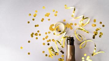 champagneflaska med gyllene konfetti-streamers på vit bakgrund