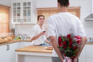 en ung HBTQ par firar de dag av kärlek med en glas av vin i deras Hem kök. med en överraskning med en reste sig från en älskare foto