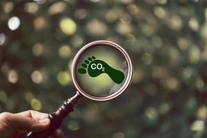 kol fotavtryck med förstorande glas på grön bakgrund. kol fotavtryck är total belopp av kol dioxid och växthus gaser sådan som metan, salpetersyra oxid gas, emitteras från tjänster. foto