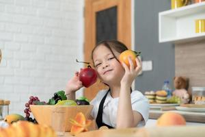 porträtt av en liten flicka i de kök av en hus har roligt spelar med frukt leksak och köksutrustning foto