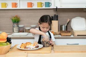 porträtt av en liten flicka i de kök av en hus har roligt spelar bakning bröd foto
