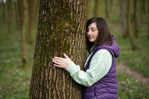 porträtt av kvinna kram och mager till träd på skog. kärlek till natur. foto