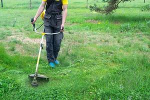 en manlig trädgårdsmästare klipper de grön gräs av de gräsmatta i de bakgård med en bensin gräsklippare. trimmer för de vård av en trädgård komplott foto