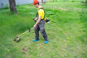 en manlig trädgårdsmästare klipper de grön gräs av de gräsmatta i de bakgård med en bensin gräsklippare. trimmer för de vård av en trädgård komplott foto