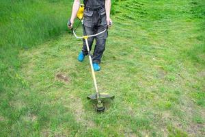 en manlig trädgårdsmästare klipper de grön gräs av de gräsmatta i de bakgård med en bensin gräsklippare. trimmer för de vård av en trädgård komplott foto