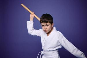 självsäker charmig europeisk krigisk konst kämpe poser med aikido trä- vapen, isolerat på lila bakgrund, kopia ad Plats för text foto