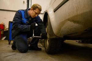 ung caucasian bil mekaniker kontroll bil hjul i bil service garage. mekanisk underhåll ingenjör arbetssätt i bil- industri. bil underhåll och reparera begrepp foto