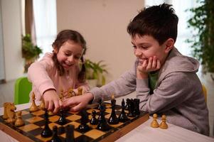 två förtjusande ungar, pojke och flicka, bror och syster har bra tid spelar schack spel tillsammans på Hem interiör. foto