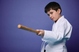 midja längd porträtt av en självsäker Tonårs pojke i vit kimono praxis trä- bokken i aikido Träning på lila bakgrund med kopia ad Plats foto