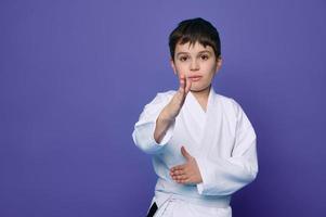 krigisk konst ge sig på. skola ålder pojke aikido kämpe i vit kimono isolerat över lila bakgrund med kopia Plats för reklam text. foto