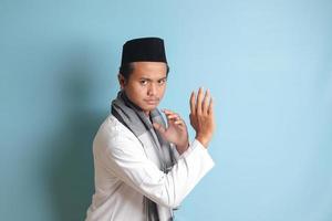 porträtt av asiatisk muslim man i vit koko skjorta håller på med krigisk konst gest eller pennkaka silat. isolerat bild på blå bakgrund foto