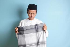 porträtt av asiatisk muslim man i vit koko skjorta hopfällbar och städa upp hans sarung . isolerat bild på blå bakgrund foto