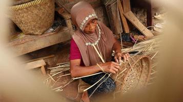 gammal kvinna hantverkare medan vävning bambu in i korgar foto