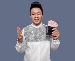 ung man är innehav och som visar en plånbok som innehåller ett hundra tusen indonesiska rupiah foto