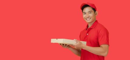 de leende pizza leverans man står på en röd bakgrund innehav de pizza låda och bär en röd keps och en tom t-shirt enhetlig. foto