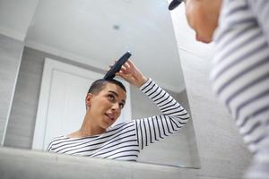 spegel reflexion av kort håriga kvinna i tank topp använder sig av hår klippning maskin foto