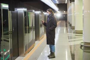 en kvinna i en medicinsk ansiktsmask väntar på ett ankommande tåg på tunnelbanan