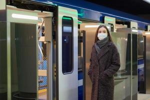 en flicka i en kirurgisk ansiktsmask håller socialt avstånd på en tunnelbanestation foto