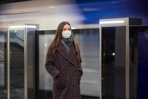 kvinna i en medicinsk ansiktsmask står nära det avgående tåget på tunnelbanan foto