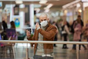 en man sätter på en mask medan han håller en kopp kaffe i köpcentret foto