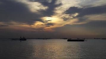 solnedgång på de hamn av industriell område, silhuett av pråm, snabb färja, stor logistisk fartyg. foto