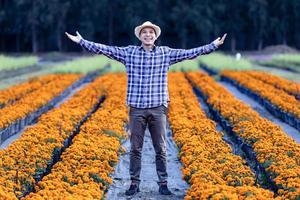 asiatisk trädgårdsmästare är välkomnande människor in i hans skära blomma bruka full av orange ringblomma för medicinsk och garnering i bra dining restaurang företag foto