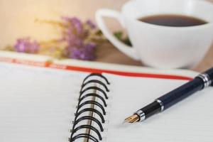 personlig arrangör eller planerare med fontän penna och varm kaffe på trä tabell. foto