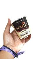 jakarta, indonesien i Mars 2023. isolerat vit Foto av en hand med en lila svartrosa konsert handledsband armband innehav en haku is grädde, ett av de is grädde Produkter produceras förbi glico vingar.