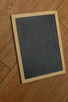 en små svart svarta tavlan med en trä- ram vilar på en trä- texturerad golv. foto