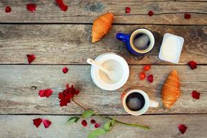 två kaffe, croissanter, socker, godis, yoghurt, reste sig och kronblad på gammal trä- bakgrund. topp se. foto